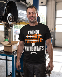 Load image into Gallery viewer, Mechanic wearing the Waiting On Parts shirt in his shop
