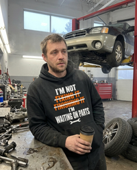 Load image into Gallery viewer, Mechanic wearing the Waiting On Parts hoodie in the shop