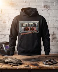 Load image into Gallery viewer, I Welded It. It Helded. welder hoodie on a workbench with a welding helmet, gloves and C-clamp