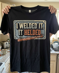 Load image into Gallery viewer, Holding up the I Welded It It Helded shirt as a gift
