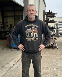 Load image into Gallery viewer, Welder wearing the Silently Judging Your Welds hoodie outside his shop