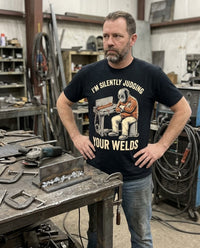 Load image into Gallery viewer, Welder wearing the Silently Judging Your Welds shirt in his shop